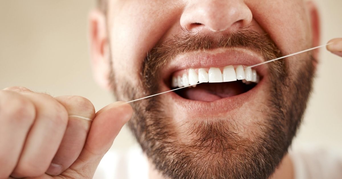 A man flossing his teeth in front of a mirror